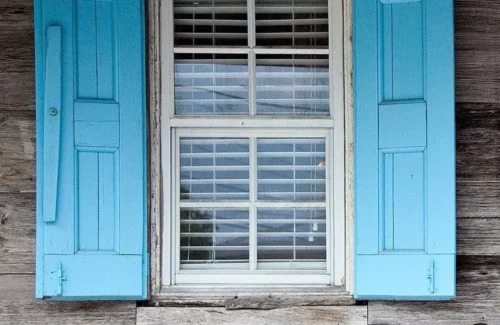 Altes Fenster in hölzerner Fassade mit blauen Klappläden in hellblauer Farbe.