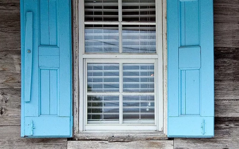 Altes Fenster in hölzerner Fassade mit blauen Klappläden in hellblauer Farbe.