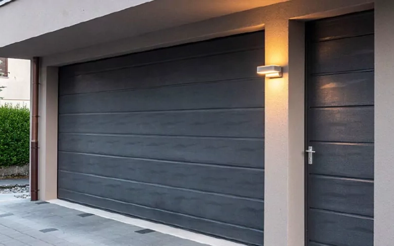 Dunkles Sektionaltor mit passender Seitentür an einer Garage.